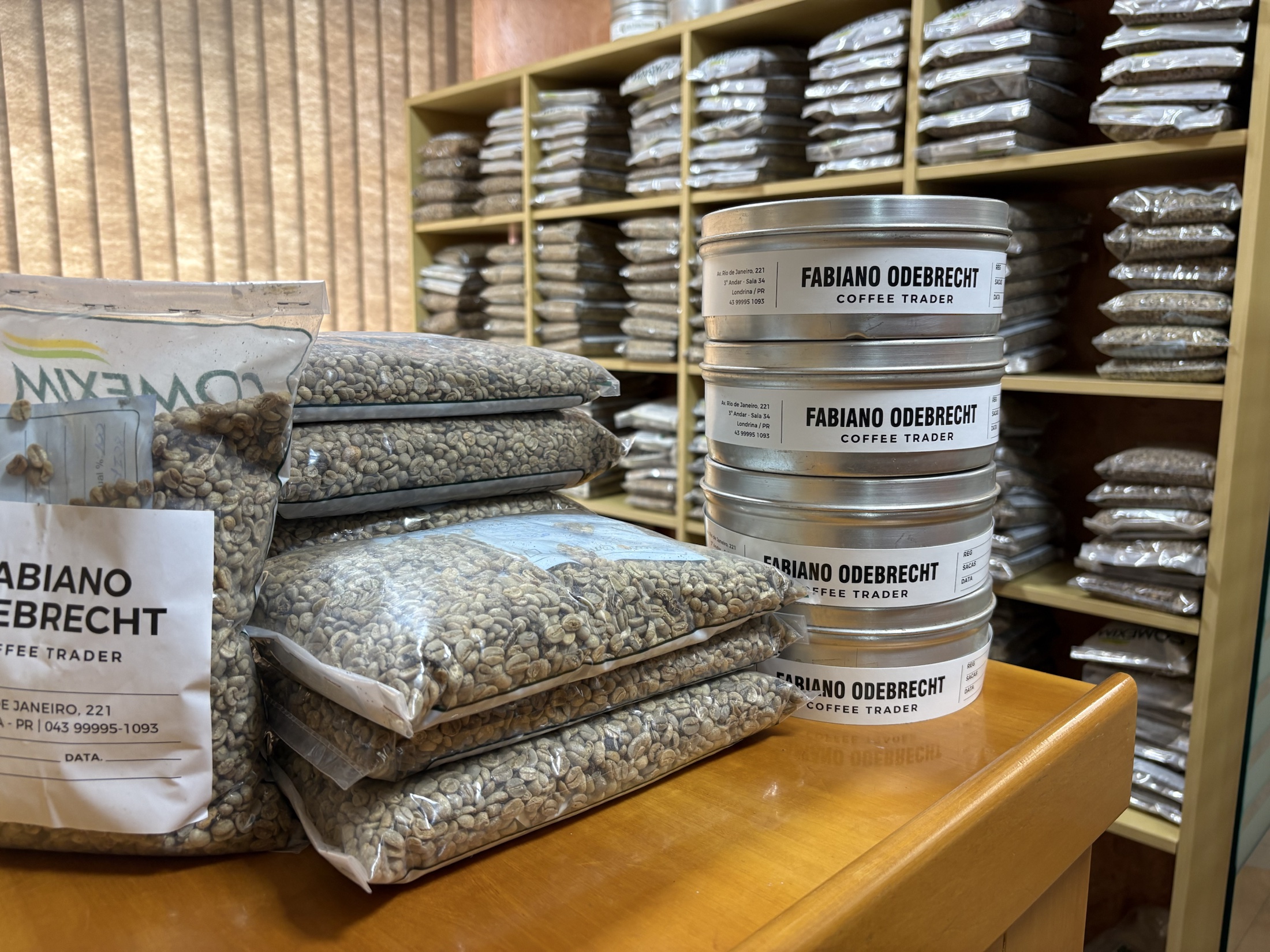 Amostras de café verde e recipientes identificados como Fabiano Odebrecht Coffee Trader em ambiente de classificação e corretagem